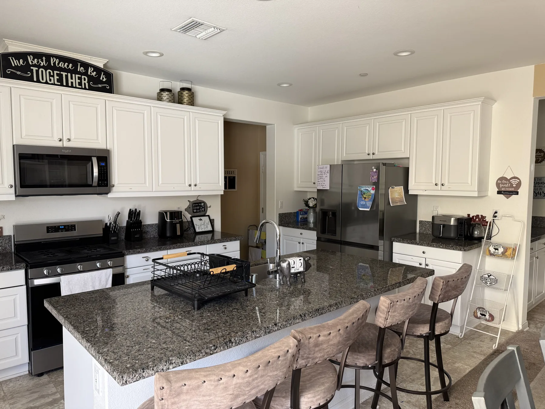 Bright open kitchen with a large granite island and seating, white cabinets, and stainless steel appliances — the heart of our Riverside recovery home.